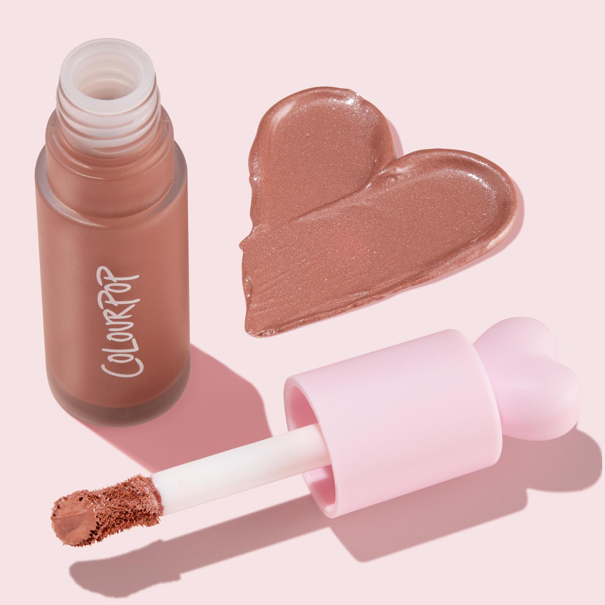 ColourPop Liquid Blush in City Walk swatches as a shimmery rosy‑nude heart beside an open frosted bottle and doe‑foot applicator with a pink heart cap, styled in a clean flat lay on a pastel pink background.