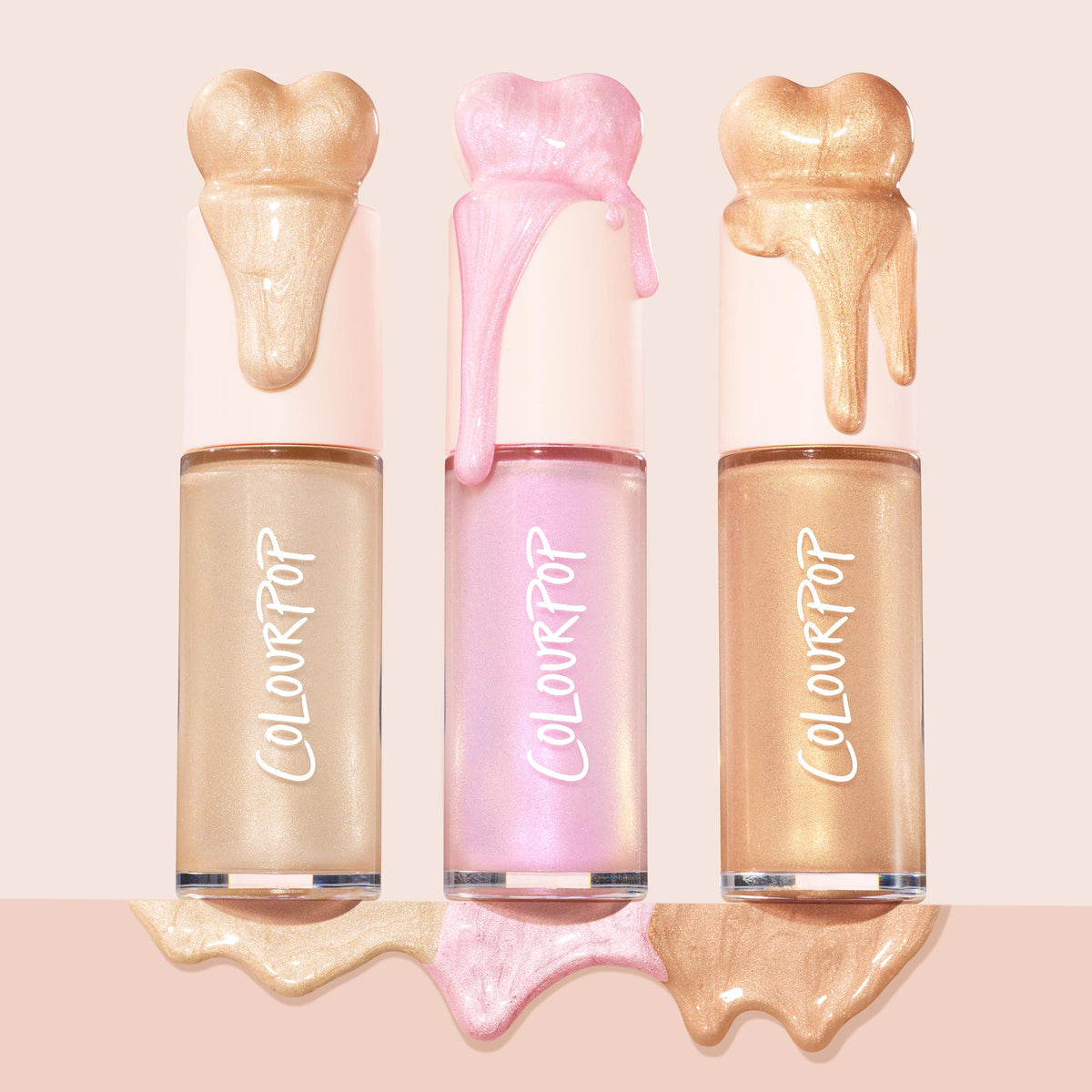 ColourPop Liquid Highlighter in Pink Pony stands centered with a glossy pink drip and pooled swatch, flanked by champagne and warm gold shades in matching tubes on a blush backdrop, showcasing an iridescent, dewy finish.
