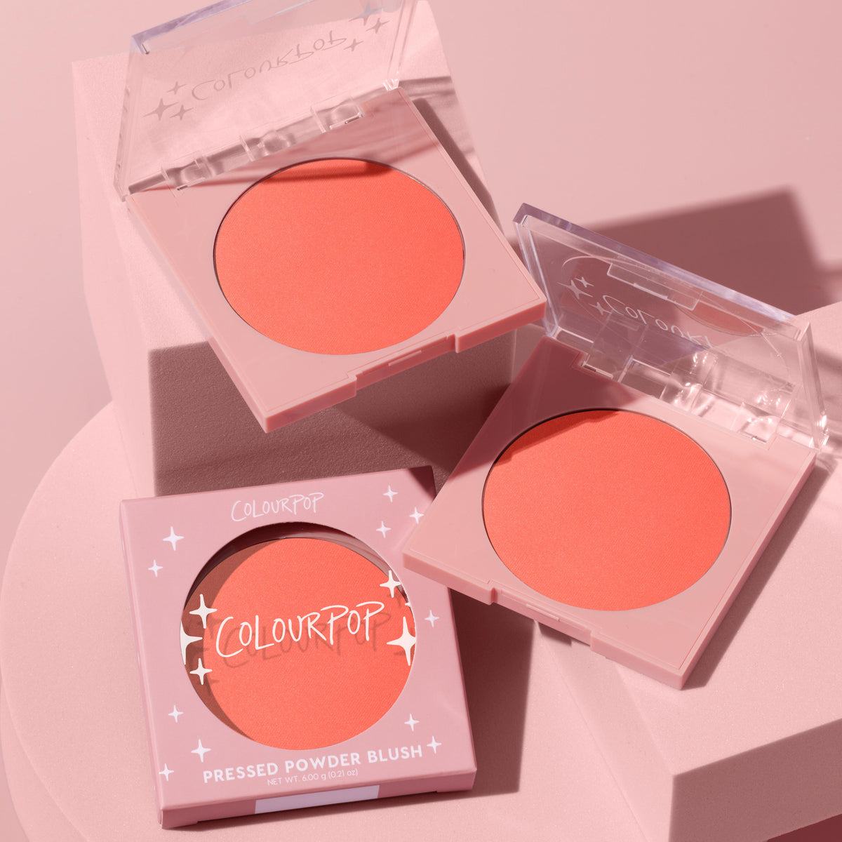 Papaya, a coral-peach ColourPop Pressed Powder Blush, displayed in two open pans and one boxed compact on soft pink blocks, clear lids with star accents catching light to show the matte finish for fresh, everyday cheeks.