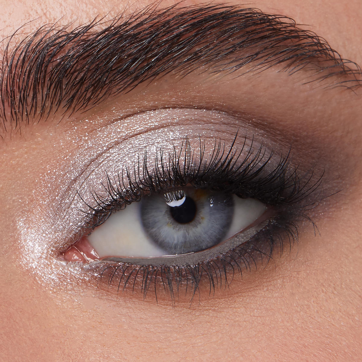Shimmery silver eyeshadow sweeps across a blue-gray eye with a soft charcoal smoked crease and inner-corner highlight, showcasing Metallic Mood ColourPop Shadow Palette & Brush Set payoff and brush-blended finish in a beauty macro.