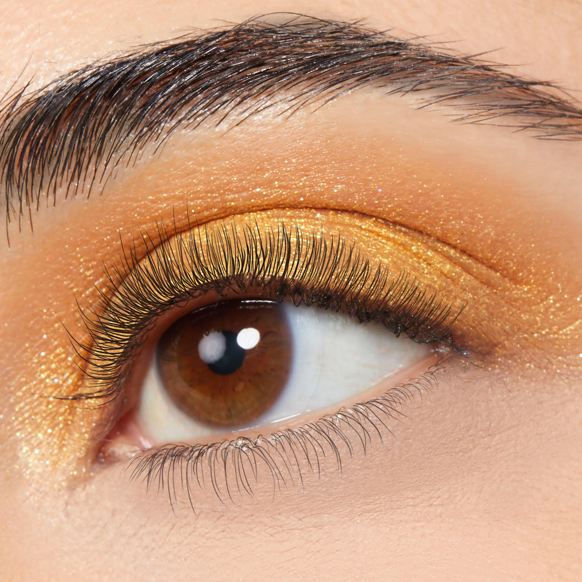Montecito Super Shock Shadow by ColourPop sweeping across a brown eye, shimmering metallic gold-orange on the lid with fine glitter, shown in a close-up wear shot with natural lashes and a groomed brow for everyday glam.