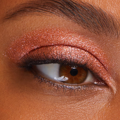 Shimmering copper eyeshadow coats a brown eye, showcasing Flamethrower, a metallic shade of ColourPop Super Shock Shadow, with glittery payoff swept across the lid and crease, accenting soft lashes and skin texture in a tight beauty close-up.