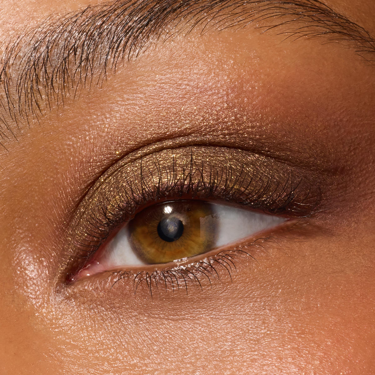 ColourPop Super Shock Shadow in We Won't Bite coats the upper eyelid with metallic olive-bronze shimmer, softly blended into the crease with fine gold sparkle, shown in a macro close-up highlighting texture and color payoff.