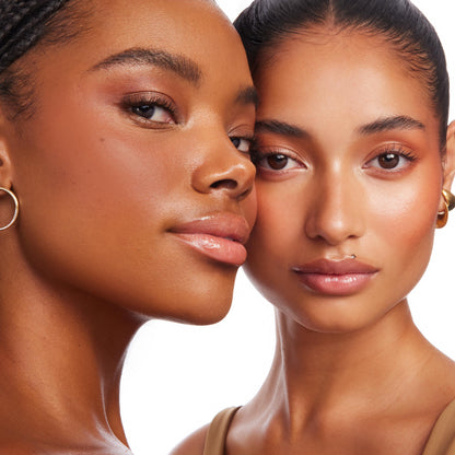 Two models showcase Laguna Beach ColourPop Bronzer Stix, wearing warm bronze on cheeks and temples for a natural, dewy glow and soft contour, glossy lips, and minimal makeup, posed cheek-to-cheek against a clean white background.