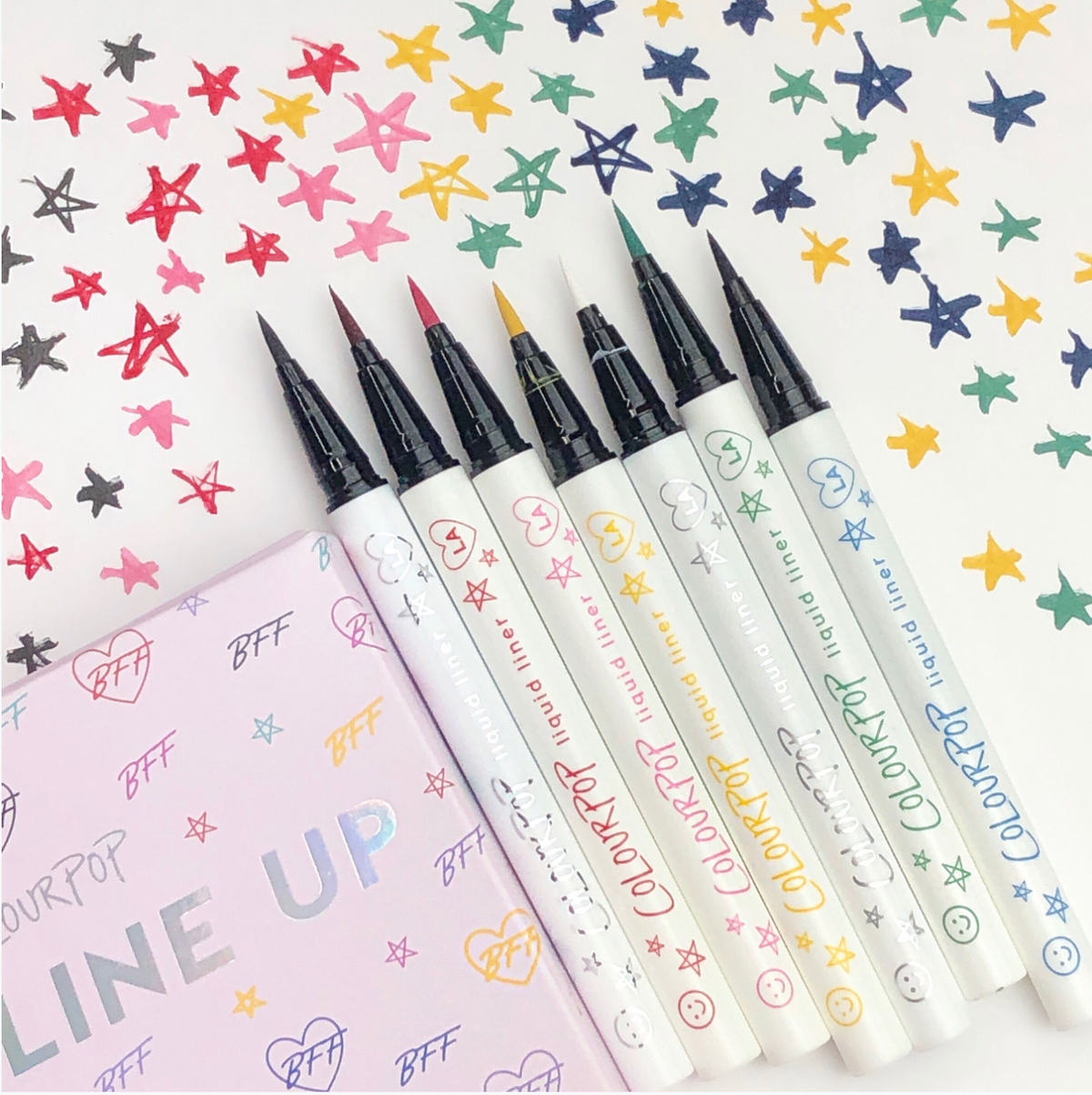 ColourPop BFF Liquid Liner The Hills shown uncapped with a fine felt tip alongside other shades, creating star swatches on white paper next to a pastel LINE UP box, showcasing the precise liquid eyeliner pen.