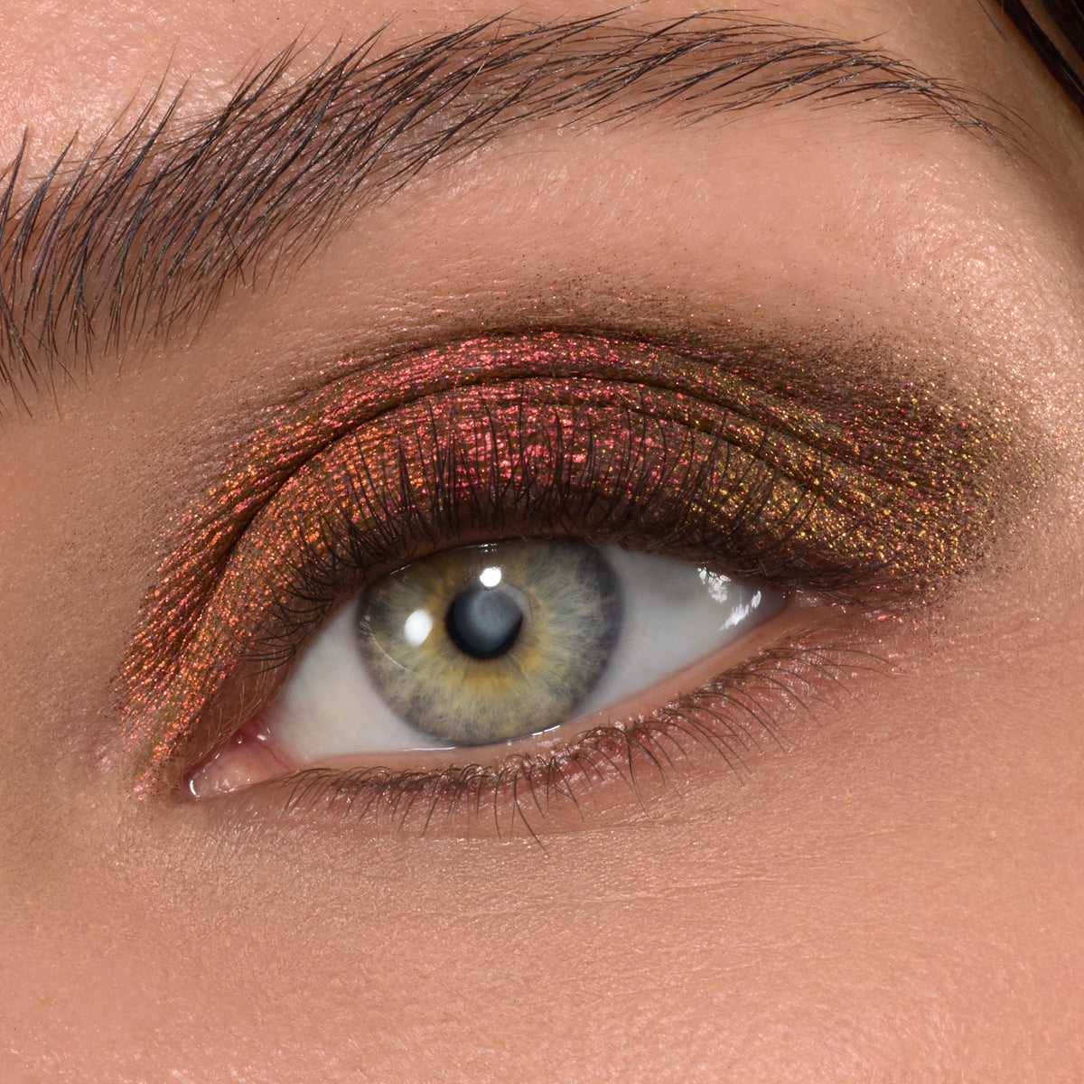 Metallic copper-red to olive-gold duochrome eyeshadow sweeps across a bare eyelid, catching light with fine shimmer, showcasing ColourPop Shadow Stix in Vampire Girl - creamy, blendable payoff in a macro close-up of an open eye.