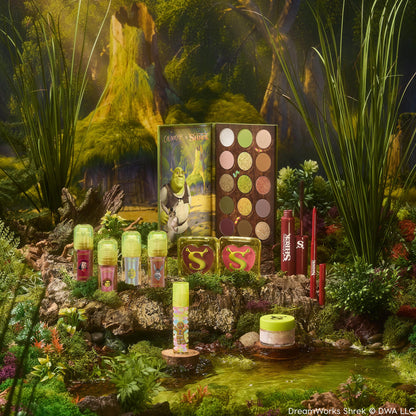ColourPop X DreamWorks Shrek Full Collection Set showcasing an open 15-pan green-and-neutral eyeshadow palette, lip products, blush compacts with S logos, eyeliner, and highlighter, styled in a mossy swamp scene; ColourPop Full Collection Set.