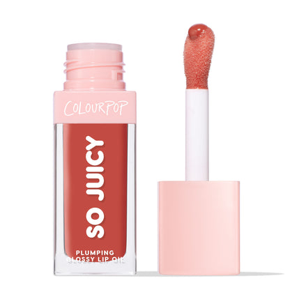 ColourPop So Juicy Plumping Glossy Lip Oil in So Sassy stands with cap off, showing doe-foot applicator loaded with warm rosy-coral tint; clear rectangular tube with pink cap and SO JUICY branding, on a white background.