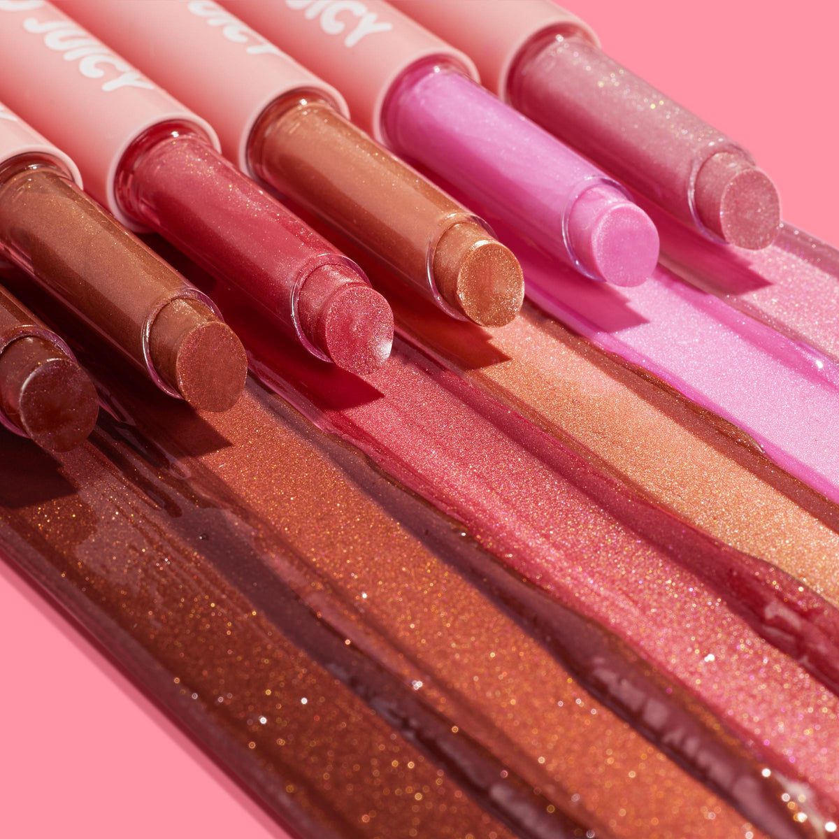 ColourPop So Juicy Plumping Gloss Balm with Peptides, Tini Time, shown with angled sticks displaying pearly high-shine swatches in warm nude, rose, and pink tones on a pink backdrop to highlight glossy payoff and texture.