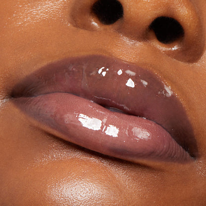 Plum-tinted lips glossed with ColourPop Lux Lip Oil, shade Vampy Lips, gleam with a glassy shine, reflecting light in an extreme close-up on warm brown skin.