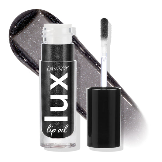 Team Jacob ColourPop Lux Lip Oil displayed open, doe-foot applicator beside the tube and a glossy charcoal-black swatch with silver shimmer behind, highlighting the sheer, high-shine finish; cap off on a white studio backdrop.