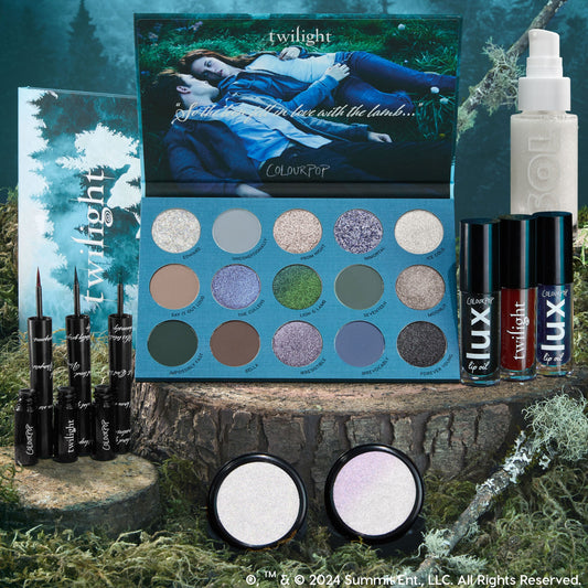 Twilight x ColourPop Full Collection Set displayed on a mossy stump, featuring a 15-pan cool-toned eyeshadow palette, three black liquid liners, three Lux lip oils, two iridescent highlighters, and a SOL shimmer body oil in forest-themed packaging.