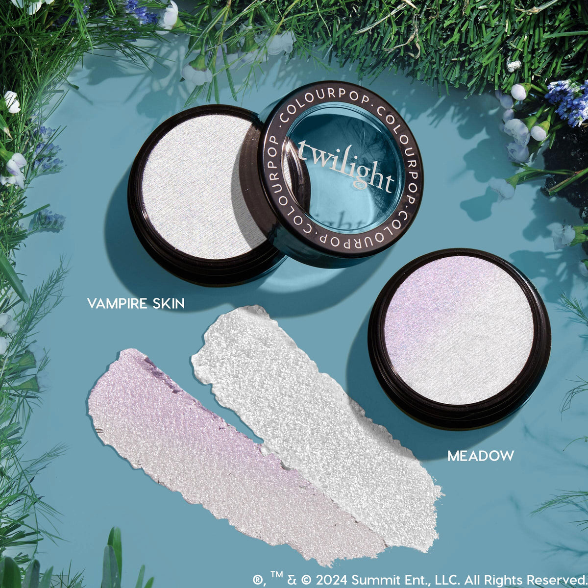 ColourPop Super Shock Highlighter Meadow - open pan showing an icy white highlighter with a lavender iridescent shift - sits beside Vampire Skin with both shades swatched below; Twilight-branded lid on a blue backdrop framed by greenery.