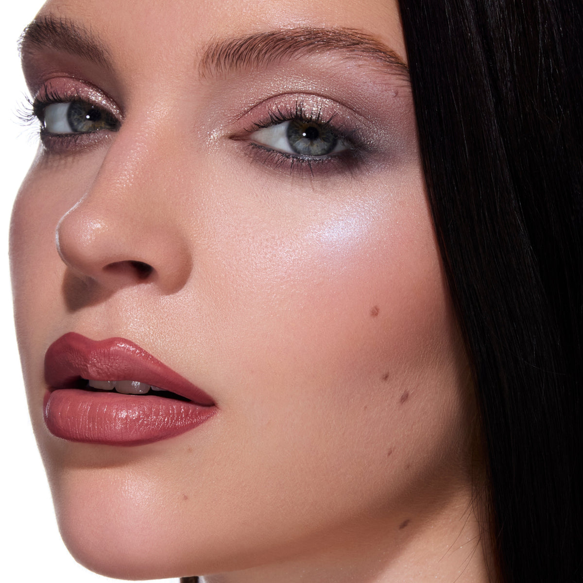 Model wearing ColourPop Change Me Mega Highlighter from the Twilight collection, showing an icy lavender glow on the cheekbone with soft mauve eyeshadow and rose nude lipstick against a clean studio background.