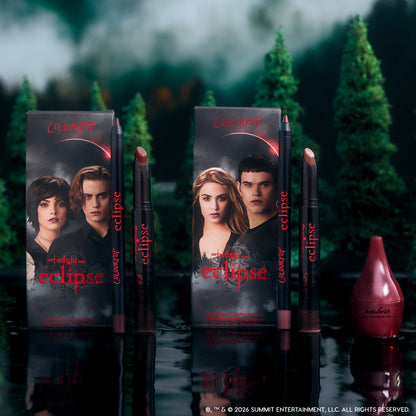 Just Bitten lip trio from the Twilight x ColourPop Eclipse collection standing upright in a dark forest setting, showing three vampy nude and berry lip pencils and sticks beside character-adorned boxes for dramatic, fandom-inspired makeup looks.