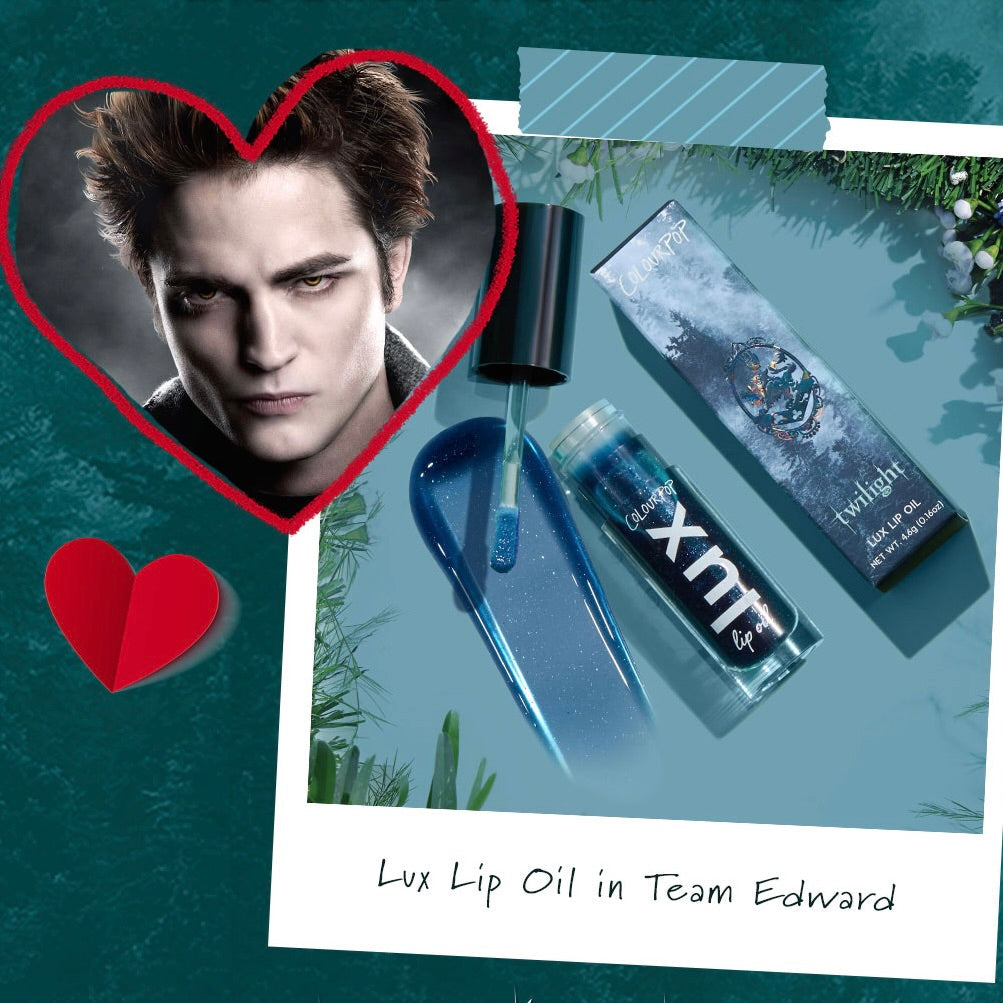 ColourPop Lux Lip Oil in Team Edward spills a glossy sheer blue swatch as the doe-foot applicator rests beside the tube and Twilight-themed box, set on a teal backdrop with a heart-framed character portrait accent.