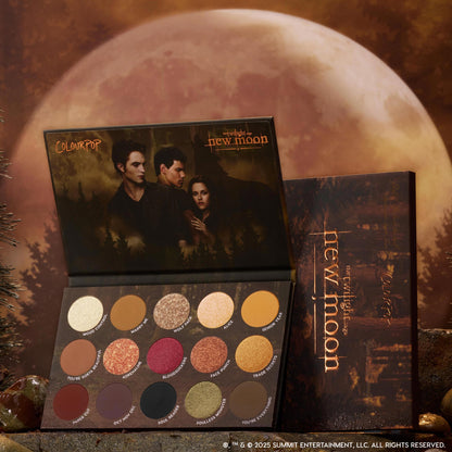 ColourPop Twilight Forever palette trio New Moon edition opened to show 15 warm-toned shimmer and matte eyeshadows arranged in rows, set against a moody full-moon forest backdrop for Twilight makeup fans in the US.