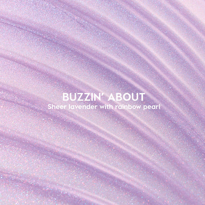 ColourPop Ultra Glossy Lip Buzzin' About swatched - sheer lavender gloss with rainbow pearl shimmer - spread in sweeping ridges across a close-up backdrop to showcase its glossy, sparkly finish.