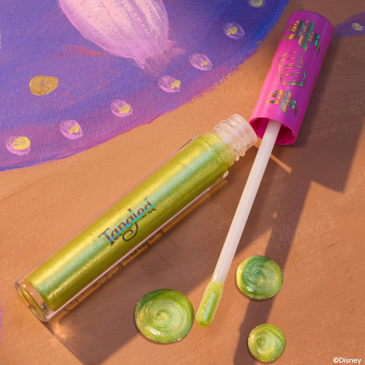 Pascal ColourPop Ultra Glossy Lip lying open with a doe-foot applicator and swirls of lime-green, gold-shimmer gloss, set on a Tangled-inspired painted backdrop, clear tube showing iridescent sheen and pink cap decorated with chameleon icons.