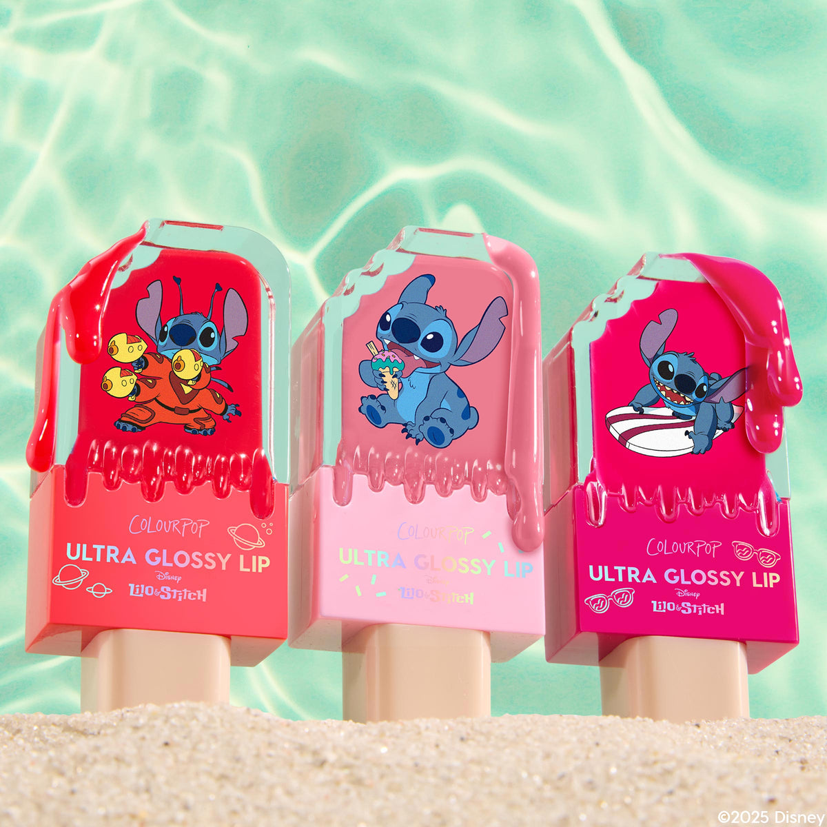 Three ColourPop Ultra Glossy Lip Keepin’ It Sweet tubes stand upright in beach sand, popsicle-shaped casings with drippy gloss and Disney Lilo & Stitch graphics in red, blush pink, and hot pink, set against turquoise pool water.