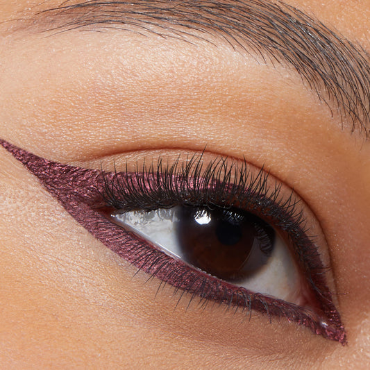 Metallic burgundy cat-eye wing on a brown eye, created with ColourPop Graphix Ink Liner in Vampire, showcasing a sharp extended wing and smooth shimmer along upper and lower lash lines in a close-up beauty shot.