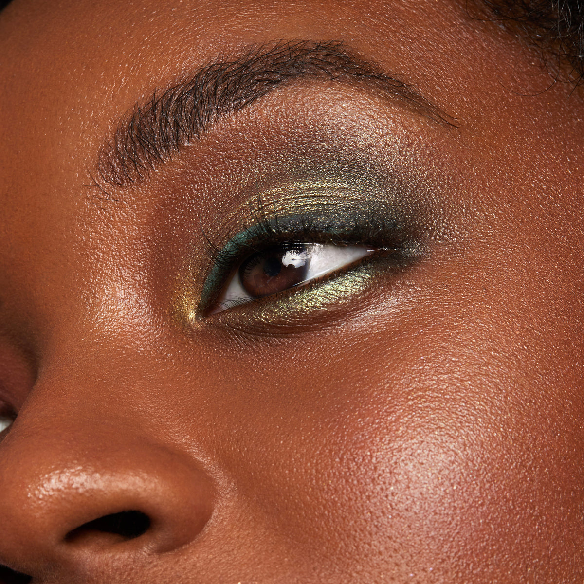 Eyelid wears ColourPop Moonwalk Super Shock Shadow, a duochrome olive-gold shimmer with green shift, blended across the lid and inner corner, highlighting metallic payoff and smooth finish in a close-up beauty swatch.