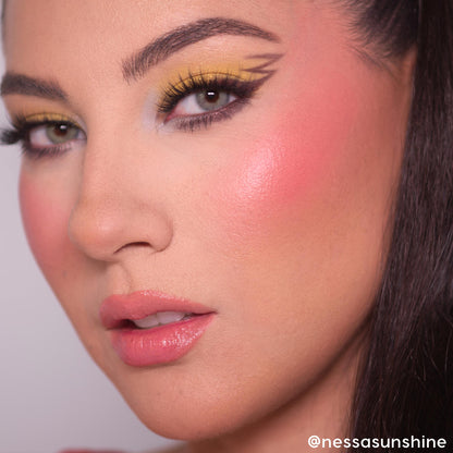 ElectroBall ColourPop Cream Blush delivering a dewy, vibrant coral‑pink flush on the cheek, showcased in a close-up with bold yellow winged eyeliner, long lashes, and glossy pink lips for a fresh, luminous finish.