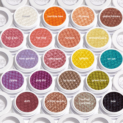 ColourPop Super Shock Shadow Pug Life, an open single pot revealing a shimmery, bold purple eyeshadow with a quilted texture, set among multiple shades in white jars in a bright overhead flat lay.